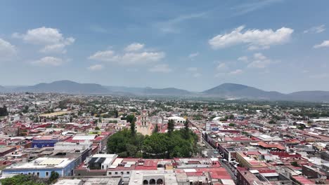 Dolly-in-flight-over-Atlixco,-Puebla-overlooking-main-park,-Saint-Mary-of-the-Nativity-Church,-city-and-mountains