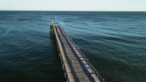 Aerial-dolly-along-abandoned-old-ocean-pier-with-sea-gull-flying-in-sky-above-open-ocean