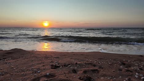 The-sun-sets-beautifully-over-the-Sea-of-Azov,-casting-vibrant-colors-across-the-water-and-illuminating-the-sandy-shoreline