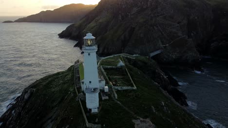 South-Stack-lighthouse-aerial-establishing-view-above-island-landmark-revealing-sunrise-mountains