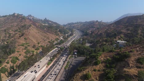 Aerial-pullback-above-bustling-highway-between-dry-arid-valleys-in-Los-Angeles-California