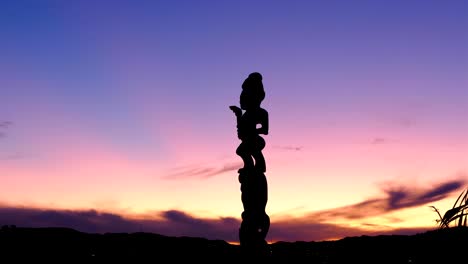 Pan-up-of-traditional-Maori-pou-whenua-carved-statue-silhouetted-against-pink-and-purple-sunset-sky-on-Mt-Vic-lookout-in-Wellington,-New-Zealand-Aotearoa