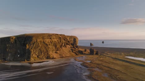 Vista-Aérea-De-Un-Vasto-Paisaje-Vacío-Con-Un-Faro-Remoto-Sobre-Una-Gran-Roca-Naranja-En-Islandia