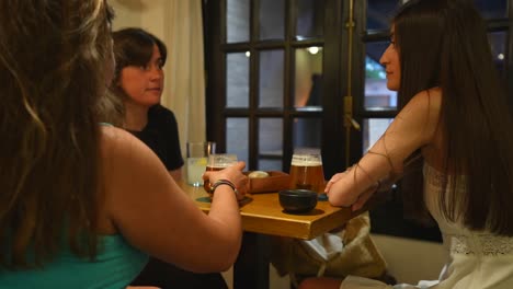 Three-women-converse-over-drinks-in-a-cozy-pub-at-night