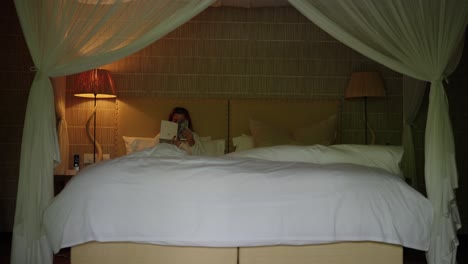 Frauen-Liegen-Im-Bett-Eines-Luxushotels-Und-Lesen-Ein-Buch-Mit-Einer-Nachttischlampe