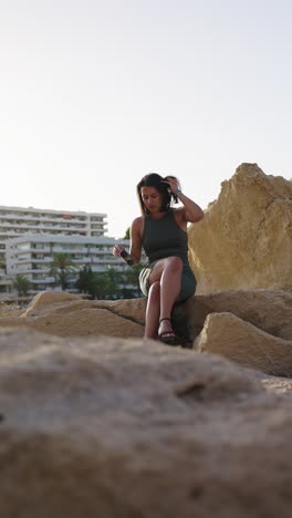 Vertical-view-of-alone-female-tourist-sit-on-large-rock,-resort-in-Mallorca