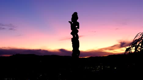 Close-up-of-traditional-Maori-pou-whenua-carved-wooden-statue-at-Mt-Vic-lookout-with-beautiful-purple-sky-sunset-in-Wellington,-New-Zealand-Aotearoa