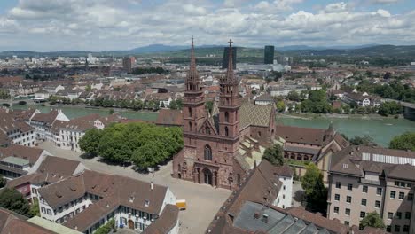 Vídeo-De-Dron-En-4K-De-Una-Iglesia-Gótica-Con-Dos-Torres-En-Basilea,-Suiza,-Con-Edificios-Modernos-Al-Otro-Lado-Del-Río-Rin