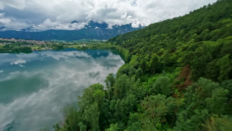 Lago-di-levico-with-lush-green-forest-and-mountains-in-the-background,-aerial-view