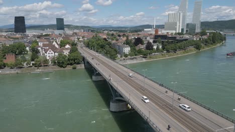 Vídeo-De-Dron-En-4K-De-Un-Remolcador-Arrastrando-Una-Barcaza-Petrolera-Bajo-El-Puente-Wettsteinbrücke-Sobre-El-Río-Rin-En-Basilea,-Suiza