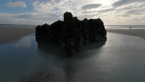 Strong-wind-creates-patterns-in-sea-water-surrounding-large-rock---Sumner-Beach,-Christchurch,-New-Zealand