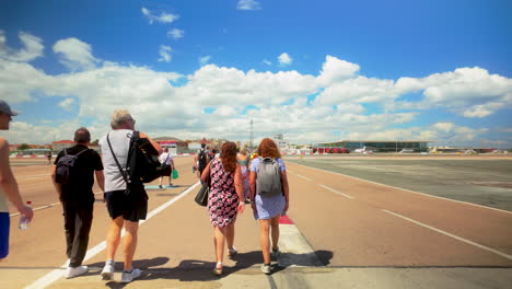 Tourists-walking-across-Gibraltar-Airport-runway-with-luggage,-sunny-day