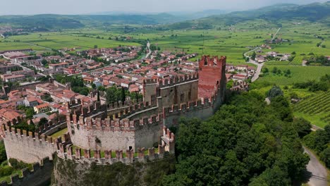 Aerial-view-of-the-medieval-scaliger-castle-in-soave,-italy,-showcasing-its-well-preserved-architecture-and-the-surrounding-vineyards