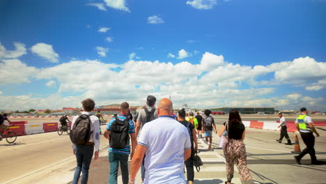 Crowd-crossing-Gibraltar-Airport's-runway,-diverse-group,-clear-day