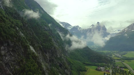 Aerial-dolly-along-steep-cliff-edge-with-clouds-rising-from-forest-trees-above-grassland-plains