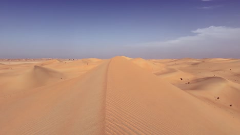 Pink-tinted-rippled-desert-sand-dunes-under-sunny-blue-sky-horizon