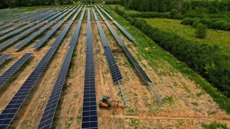 Grandes-Conjuntos-De-Paneles-Solares-En-Una-Granja-Solar,-Con-Una-Excavadora-Operando-Cerca---Toma-De-Dron-En-órbita