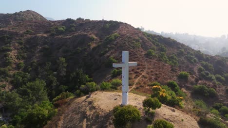 Drone-dolly-to-white-cross-on-hill-with-hiking-trail-over-dry-arid-landscape-in-foothills-of-Los-Angeles-California