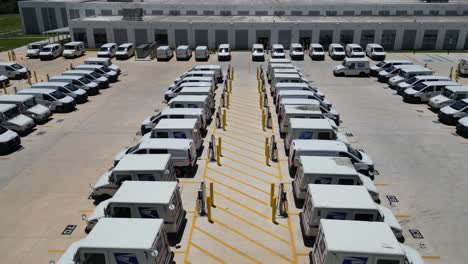 Slowly-dropping-drone-shot-of-USPS-delivery-trucks-next-to-newly-installed-chargers-behind-large-post-office-viewed-from-the-center-of-a-row-of-trucks