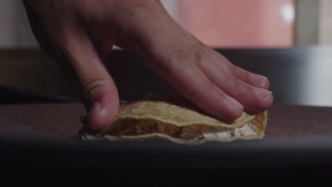 Beautiful-slow-motion-close-up-shot-of-a-professional-chef's-hand-folding-a-Mexican-tortilla-in-half-as-a-presentation-for-the-dish-of-enchiladas-in-green-sauce