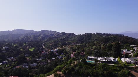 Vista-Aérea-De-Un-Pintoresco-Vecindario-En-La-Ladera-De-Una-Colina-Con-Casas-Lujosas,-Rodeadas-De-Exuberante-Vegetación-Y-Con-Un-Impresionante-Telón-De-Fondo-De-Montaña.