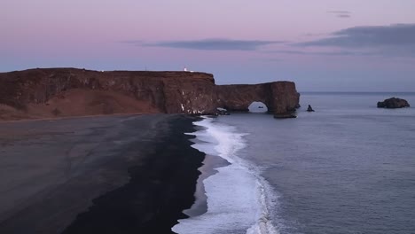 Blaue-Stunde,-Berühmter-Felsbogen-Mit-Weißem-Leuchtturm-In-Island,-Drohnen-Dolly-Draußen