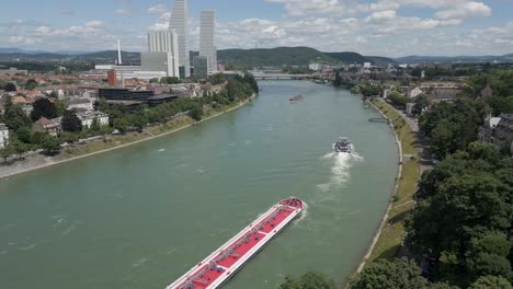 4K-Drone-Video-of-Tugboat-Pulling-Cargo-Barge-Under-the-Wettsteinbrücke-Bridge-over-the-Rhine-River-in-Basel,-Switzerland