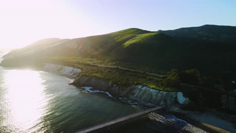 Panoramic-aerial-pullback-at-sunrise-reveals-public-pier-stretching-into-water-with-sandy-beach-below-railroad-tracks