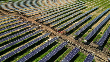 Drone-rising-backwards-over-a-solar-farm-under-construction,-sunny,-summer-day