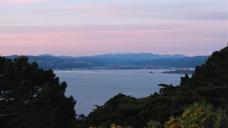 Aerial-view-overlooking-Wellington-harbour-and-snow-capped-Tararua-Range-mountains-during-pink-hazy-sunset-in-Wellington,-New-Zealand-Aotearoa