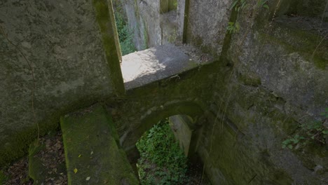 Ruinas-De-Piedra-Cubiertas-De-Musgo-En-El-Convento-De-São-Francisco-Do-Monte,-Con-Un-Pasaje-Arqueado-Que-Conduce-A-áreas-Cubiertas-De-Vegetación-Debajo.