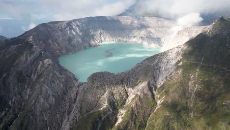 Aerial-Circling-The-Rim-Of-A-Steaming-Volcano-Ijen-with-a-Turquoise-Lake,-and-foggy-cloudy-Mountain-in-the-background---East-Java,-Indonesia