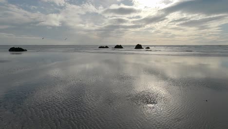 Sunlight-filters-through-clouds-illuminating-interesting-patters-in-sand-on-a-windy-day-in-winter---Sumner-Beach,-Christchurch,-New-Zealand