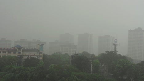 A-misty-urban-scene-with-several-high-rise-buildings-partially-obscured-by-fog,-a-school-building-in-the-foreground,-and-trees-scattered-throughout-the-landscape