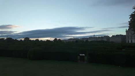 Silhouette-view-of-the-Tuileries-Garden-during-sunset-with-green-hedges-and-local-buildings-in-the-background-in-Paris,-France