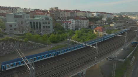 Static-shot-of-a-blue-train-on-the-train-tracks-passing-in-Prague-at-sunset-from-above,-copy-space