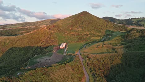 Lush-green-hills-and-a-mountain-at-sunset-near-mosteiros,-azores,-aerial-view