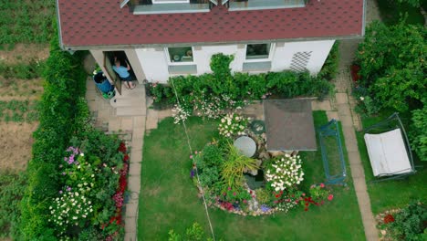 A-top-down-drone-view-of-two-men-exiting-a-house-and-walking-into-a-vibrant-garden-filled-with-flowers