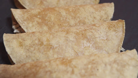 Beautiful-slow-motion-shot-panning-up-close-of-a-set-of-tacos-or-Mexican-tortillas-from-the-plate-of-chicken-enchiladas-in-green-sauce-in-a-restaurant-kitchen-on-a-black-plate