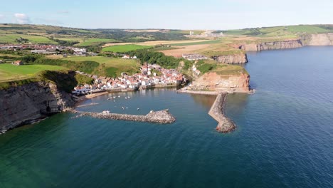 Aerial-drone-view-of-Staithes-Harbour-on-the-North-Yorkshire-coast-with-river,houses,-boats-on-a-sunny-morning-in-August,-summertime