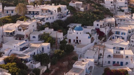 White-block-homes-with-flat-roofs-and-blue-tops-of-sacred-building-at-early-morning-in-Donousa-Greece,-aerial