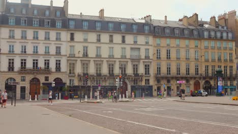 Motion-video-capturing-Typical-French-architectural-buildings-in-front-of-street-with-cyclists-cycling-in-Paris,-France