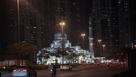 Mosque-in-middle-of-Dubai-UAE-illuminated-by-lights-cast-on-white-building-in-middle-of-downtown-cityscape-at-night