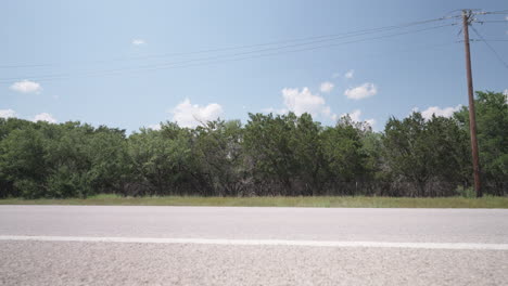 A-red-SUV-drives-past-on-a-sunny-highway-in-the-Texas-Hill-Country--slider-right-to-left