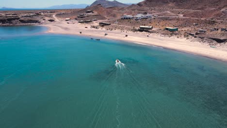 Drone-rises-behind-speedboat-landing-on-sandy-shore-of-Baja-Mexico-in-stunning-clear-green-water