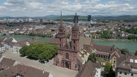 4K-Drone-Video-of-Gothic-Church-with-Twin-Bell-Towers-in-Basel,-Switzerland-with-Modern-Buildings-across-the-Rhine-River