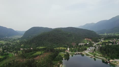 Vista-Aérea-Desde-Un-Dron-Sobre-El-Lago-Bohinj-En-Eslovenia-Con-Una-Iglesia-De-Fondo-Durante-La-Noche