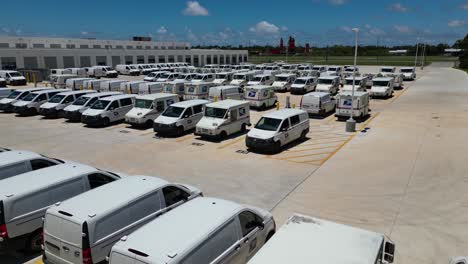 Toma-Panorámica-Lenta-De-Derecha-A-Izquierda-De-Camiones-De-Reparto-De-USPS-Junto-A-Cargadores-De-Vehículos-Eléctricos-Recién-Instalados-Detrás-De-Una-Gran-Oficina-De-Correos,-Vistos-Desde-La-Esquina-Del-Estacionamiento