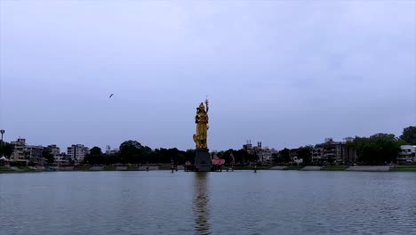 Wide-view-static-shot-on-the-Sursagar-lake-with-the-golden-statue-in-Vadodara,-India-on-a-grey-day,-copy-space