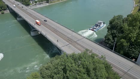 4K-Drone-Video-of-Tugboat-Pulling-Oil-Barge-Under-the-Wettsteinbrücke-Bridge-over-the-Rhine-River-in-Basel,-Switzerland